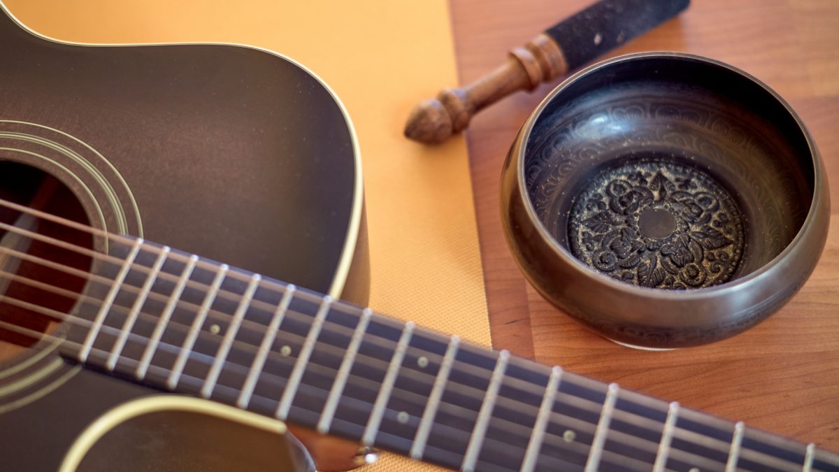Auf einer Yga-Matte liegende Gitarre, daneben eine Klangschale